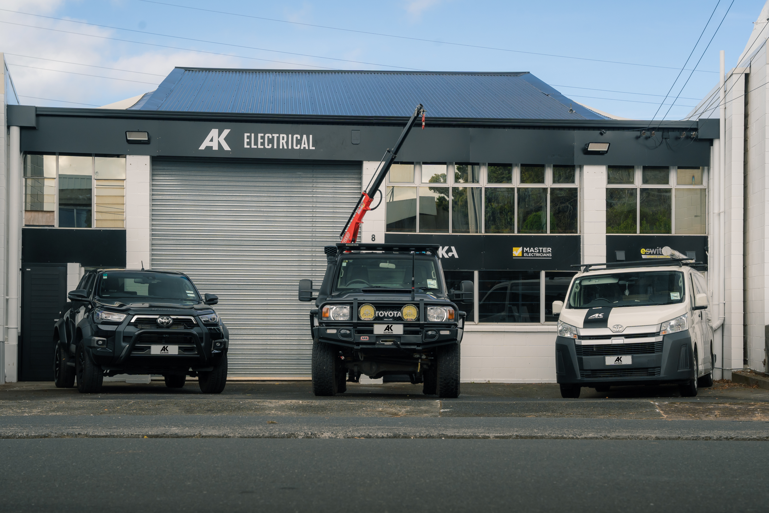 AK Electrical's Onehunga workshop with three branded work vehicles outside.