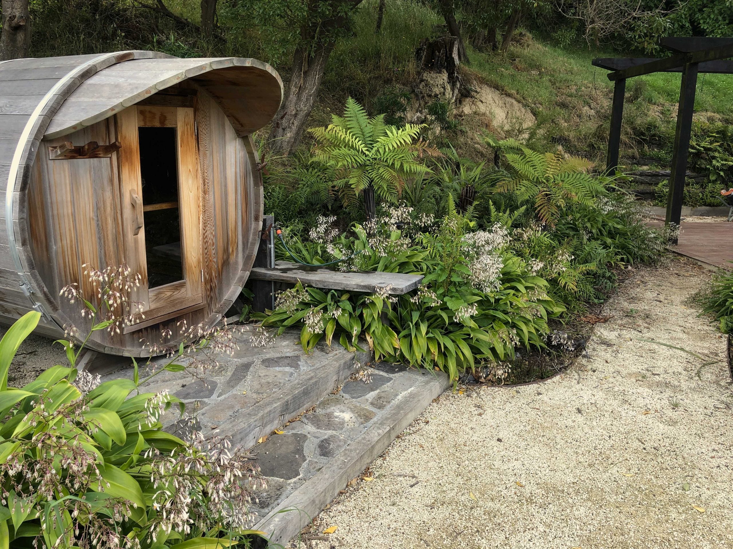 Timber sauna beside ferns, flowering plants and a gravel garden path