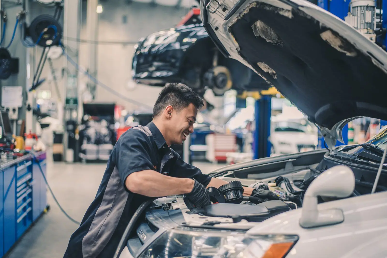Mechanic working under the bonnet of a car in an automotive workshop